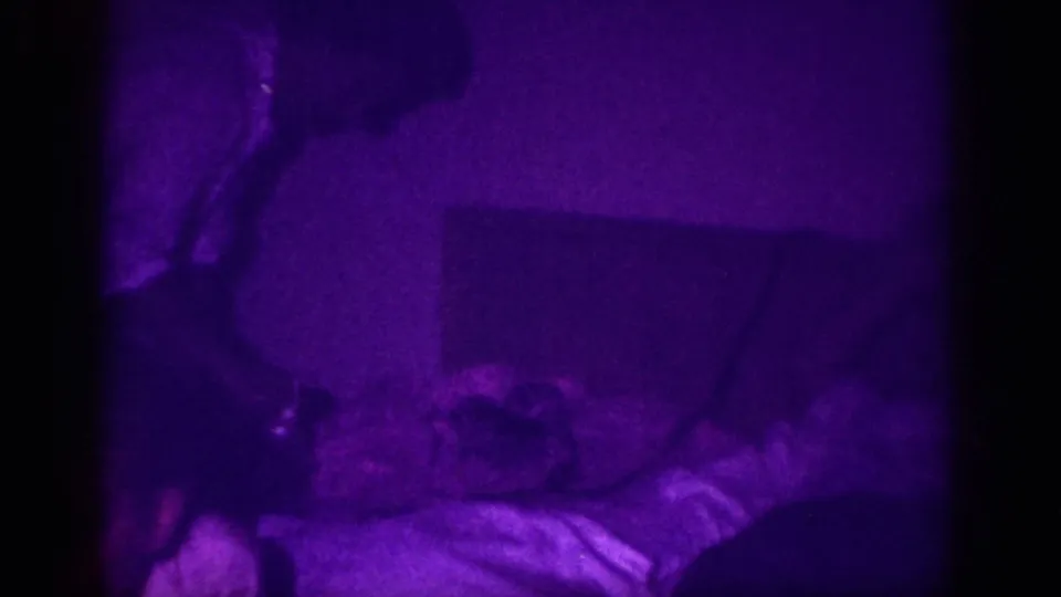 8mm home movie frame, ca. 1963, Memphis, Tennessee; purple-saturated dim interior showing clothing or fabric on a flat surface with a partial figure in the upper portion.