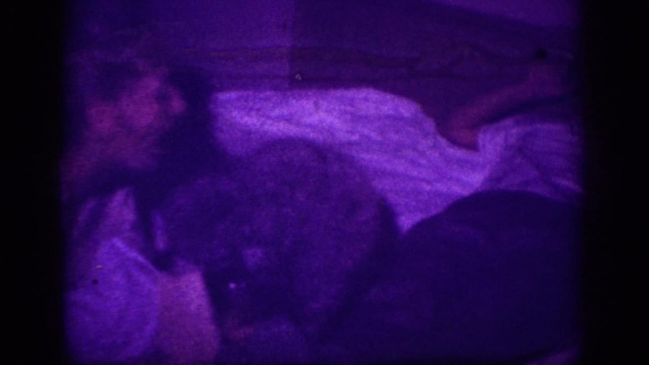 Close view of person lying in bed with white blanket and dark form possibly a dog, under intense purple color cast.