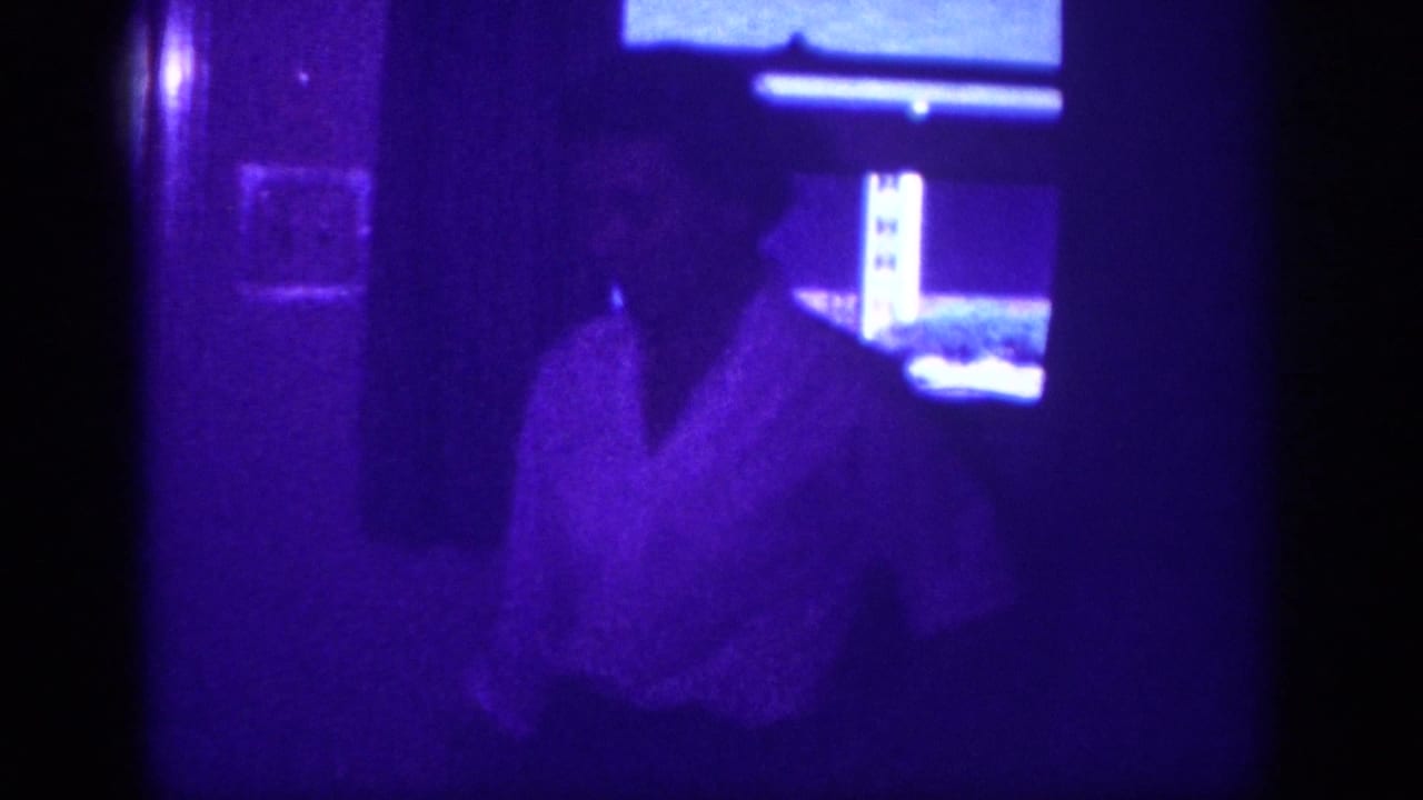 Man in white shirt walking into a purple-lit domestic interior; 8mm home movie footage attributed to Memphis, Tennessee, circa 1963.