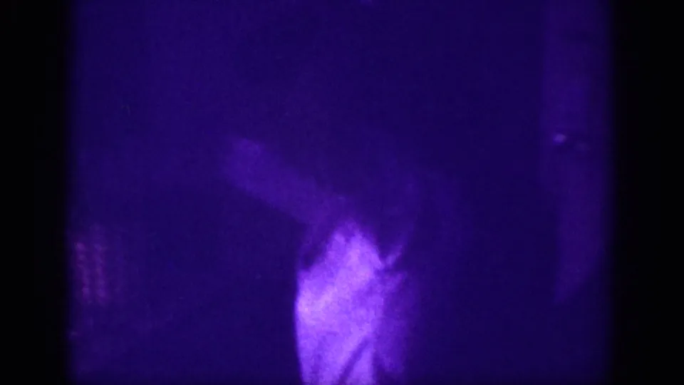 Woman bending or adjusting posture in a domestic interior, captured on aged 8mm film with heavy purple dye cast and slight motion, circa 1963.