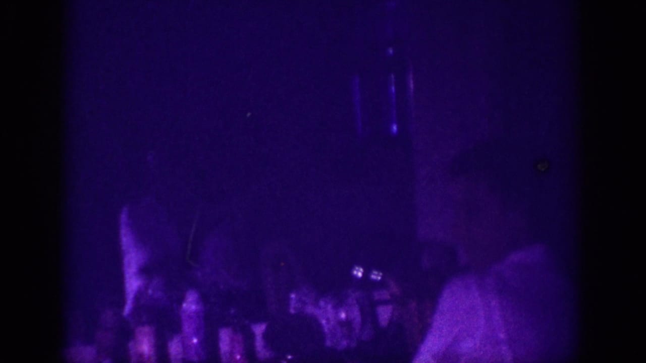 Woman's upper body visible on the right, small bottles on a counter to the left, deep purple blacklight filling the entire dark interior.