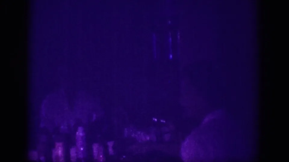 Heavily underexposed 8mm home movie frame from 1963 Memphis, showing near-total darkness with faint purple UV tones and minimal discernible shapes.