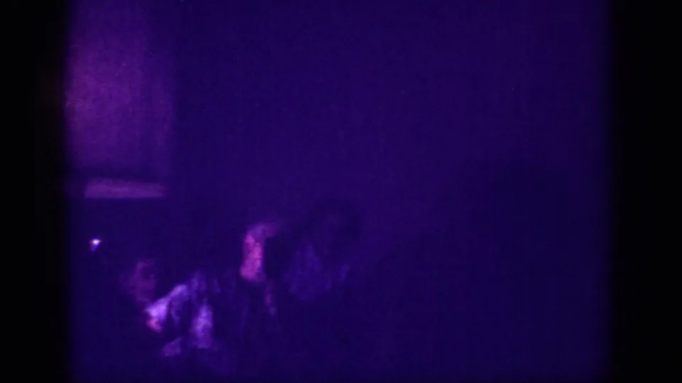 Two or three silhouetted people gathered in a darkened club interior lit by deep purple ambient light, 8mm footage Memphis 1963.