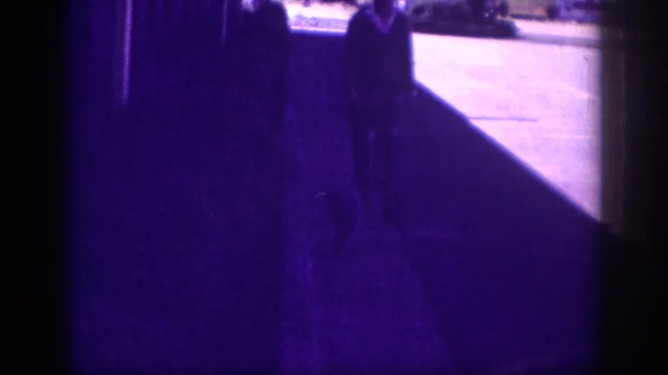 8mm cut between a dark purple-tinted interior and a sunlit residential sidewalk; a dark-clothed figure, background street, and trees are visible at right. Memphis, Tennessee, circa 1963.