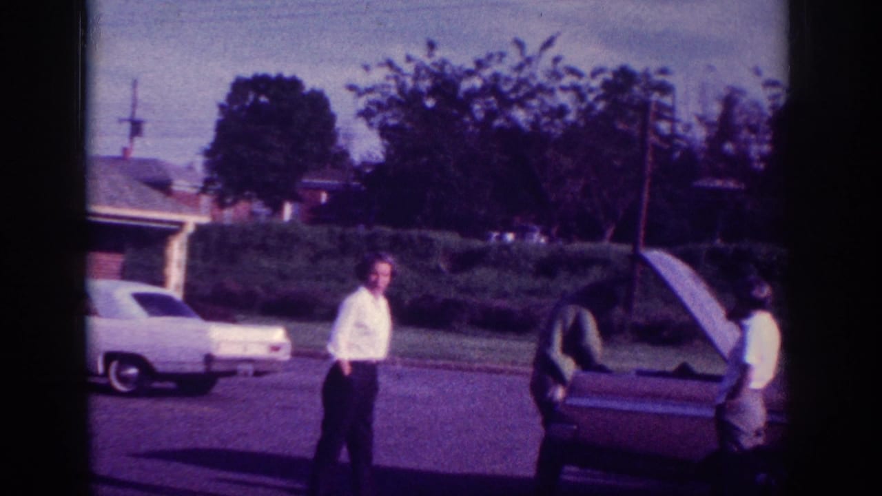 Two women in white shirts and dark pants beside a 1960s American sedan with open trunk in a suburban driveway, Memphis Tennessee, 1963