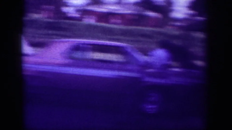 A motion-blurred handheld frame shows the long car and residential greenery passing through the view as the camera shifts quickly.