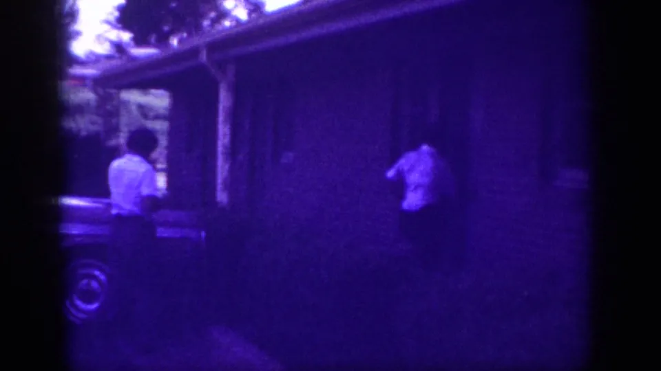Two adults in light shirts walking toward a ranch house entrance, Memphis Tennessee circa 1963; strong purple dye-fade cast from aged 8mm film.