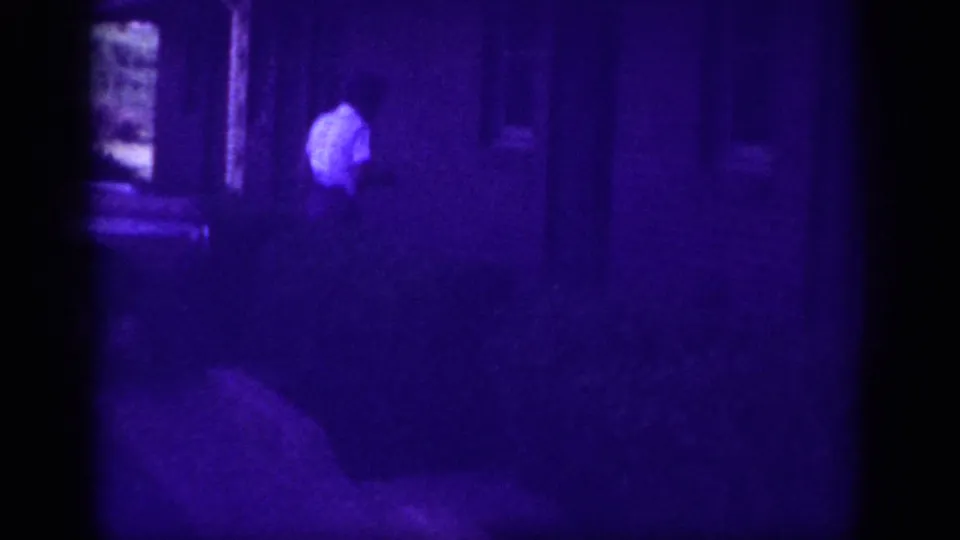 One adult in a white shirt at a house doorway, Memphis Tennessee circa 1963; heavy purple dye-fade and dark exposure from aged 8mm film.