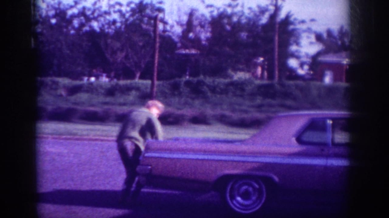 Woman leaning over the trunk of a large American sedan; car tail section and hubcap visible; heavy purple color cast.