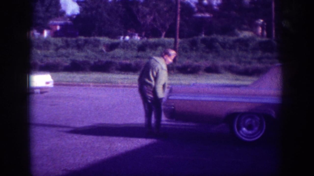 Woman in dark jacket at the open trunk of a large American sedan, filmed on 8mm in what metadata identifies as Memphis, Tennessee, circa 1963.