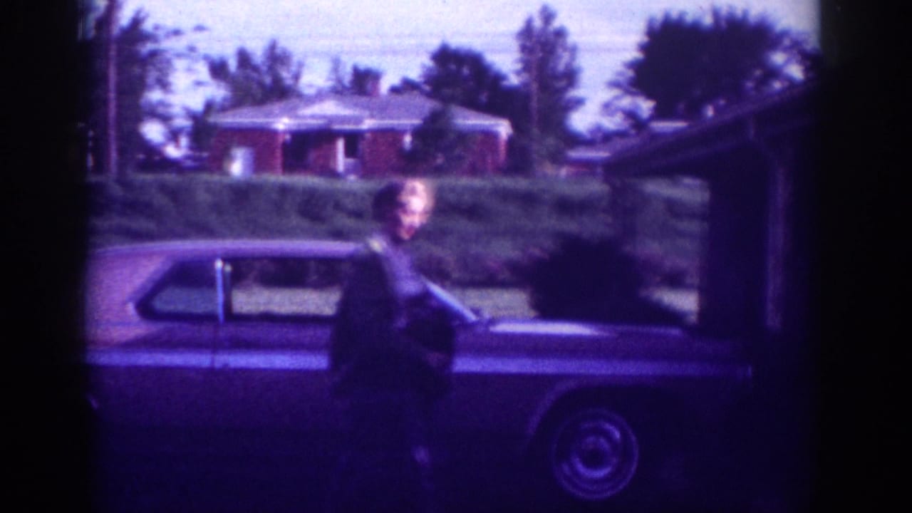 Woman in dark jacket beside an early-1960s full-size American sedan in a suburban driveway; brick ranch house and trees in background; Memphis, Tennessee area, 1963.