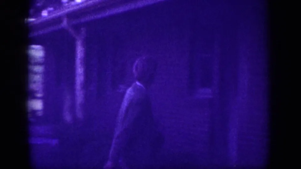 Woman walking toward a residential building in Memphis, Tennessee, 1963 home-movie footage; strong blue-violet dye shift from film aging renders the scene largely in silhouette.