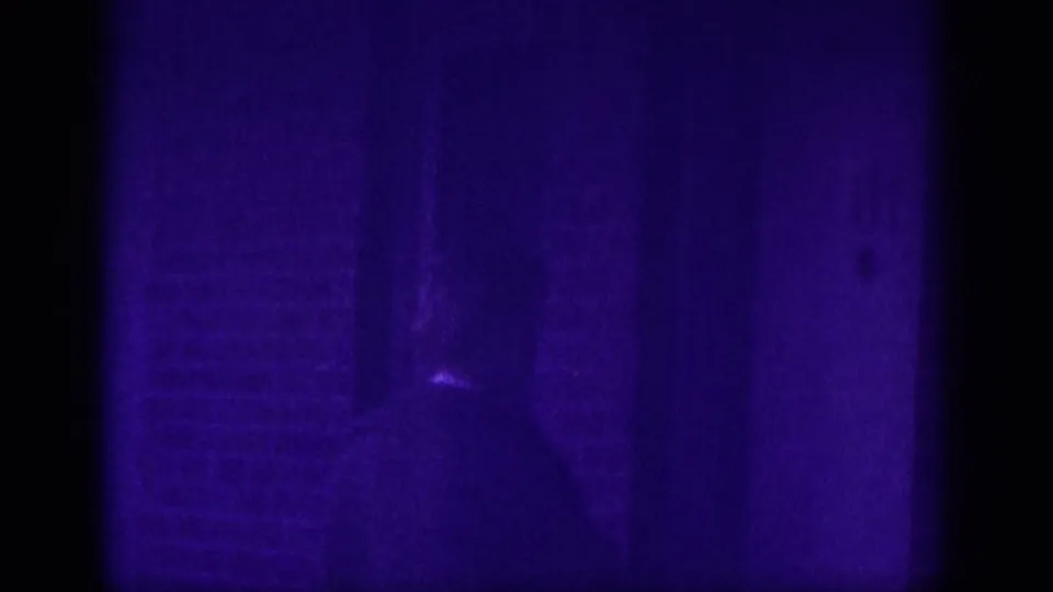 Near-dark frame from a 1963 Memphis home movie; faint figure silhouette in driveway area with heavy age-related dye degradation across 8mm stock.
