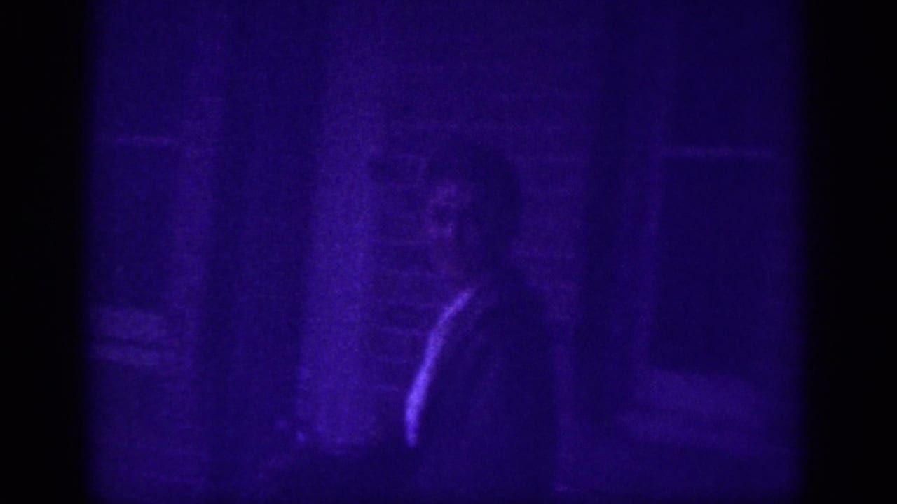 Partially visible man in dark clothing near a brick wall or doorway, rendered in heavy purple dye-shift on 8mm film, Memphis street scene circa 1963.