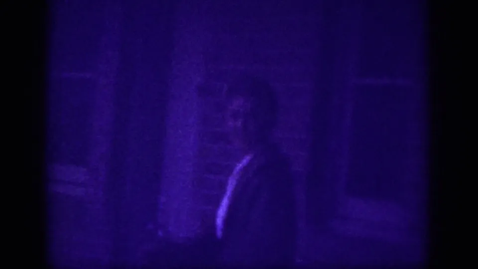 Partially visible man in dark clothing near a brick wall or doorway, rendered in heavy purple dye-shift on 8mm film, Memphis street scene circa 1963.