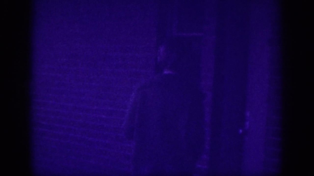 Near-black frame with a faint dark silhouette visible at top against a deep purple field on aged 8mm film.