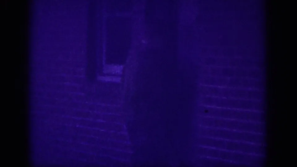 Dark silhouette of a figure standing or walking beside what appear to be steps or a sidewalk with horizontal lines, in purple-cast 8mm footage from a Memphis street scene circa 1963.