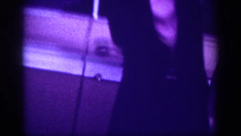 Street-level shot showing a bright horizontal element, possibly a vehicle bumper or curb edge, and a silhouetted figure at frame right, in purple-shifted 8mm from a Memphis street scene circa 1963.