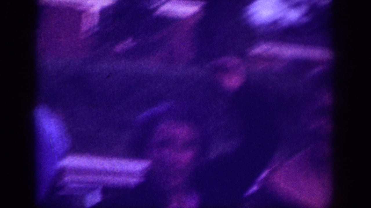 Opening frame of a 1963 8mm home movie: a motion-blurred figure in dark clothing with extreme purple-blue dye-fade and overexposed edges.