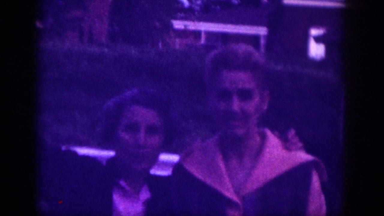 Two women facing the camera, one raising a hand to wave, wearing color-block jackets, strong purple-blue cast.
