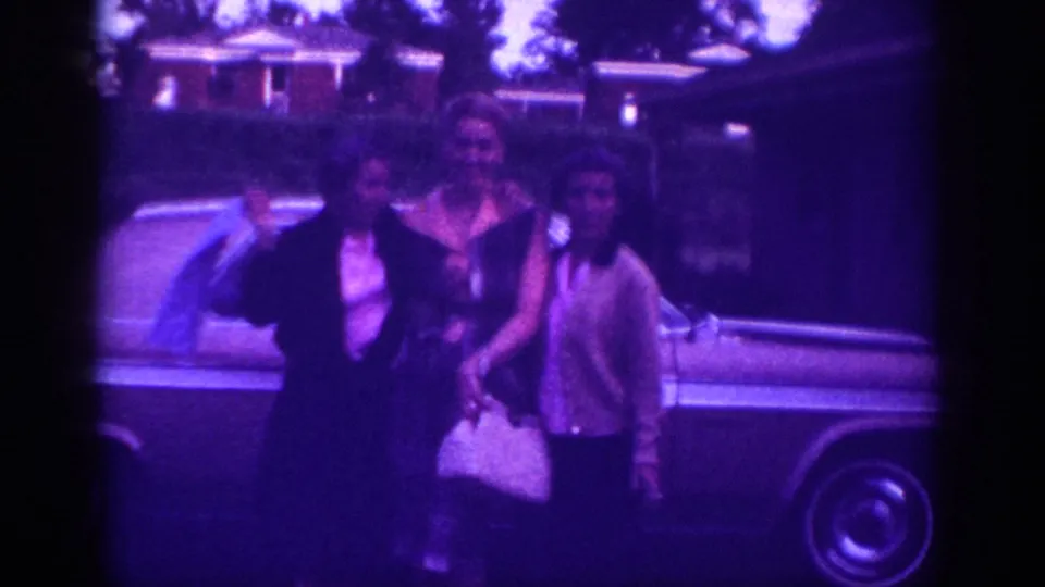 Three women in 1960s attire pose beside a large American sedan in a Memphis, Tennessee suburban neighborhood, c.1963; chrome hubcap visible in lower foreground.