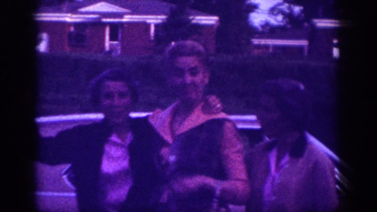 Two women posing together outdoors in front of a brick ranch house, Memphis, Tennessee, circa 1963, on heavily purple-shifted 8mm home-movie film.