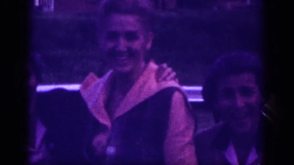 Two women caught mid-embrace in what appears to be a car-side reunion, circa 1963 Memphis, Tennessee; heavy purple dye-fade and grain from 8mm stock.