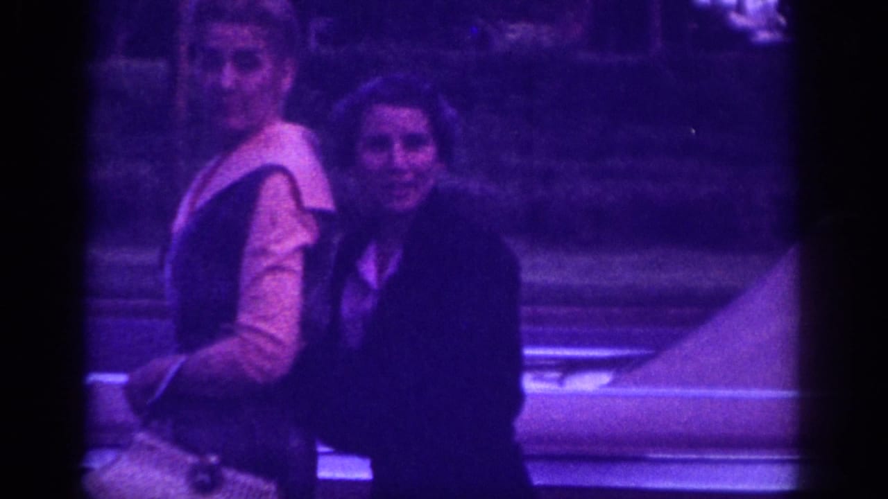 Two women pausing on a street in what appears to be Memphis, Tennessee, circa 1963; 8mm home movie with heavy purple dye shift.