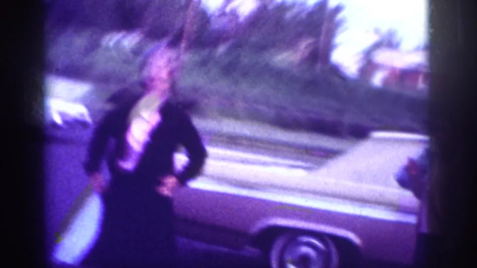 A woman in motion beside a large classic American car with whitewall tire; Memphis, Tennessee area, circa 1963, 8mm home movie.