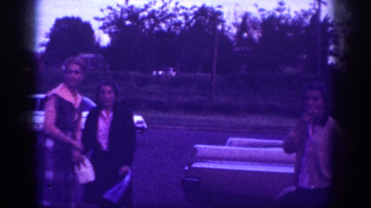 Three women in early 1960s clothing gathered in a suburban driveway, possibly Memphis Tennessee circa 1963; strong purple dye-shift on aged 8mm stock.