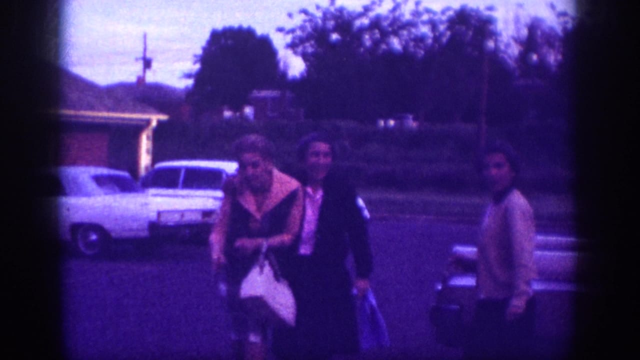 Three women standing in a driveway with a large white American sedan visible behind them, purple-magenta color cast.