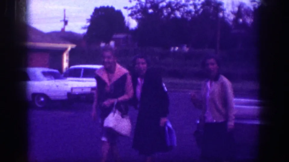 Three women near a white full-size American sedan in a residential driveway, likely Memphis Tennessee circa 1963; heavy purple dye-shift typical of aged 8mm stock.