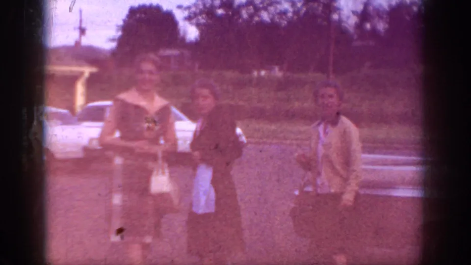 Two women prominently in foreground in period blouses with handbag, warm amber color shift in final frames; white sedan behind, likely same Memphis driveway scene circa 1963.