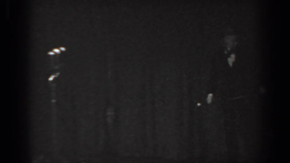 Final frame of 8mm clip from a 1965 Saint Louis tap dance performance, showing the performer at lower right and a microphone stand against a nearly black stage backdrop.