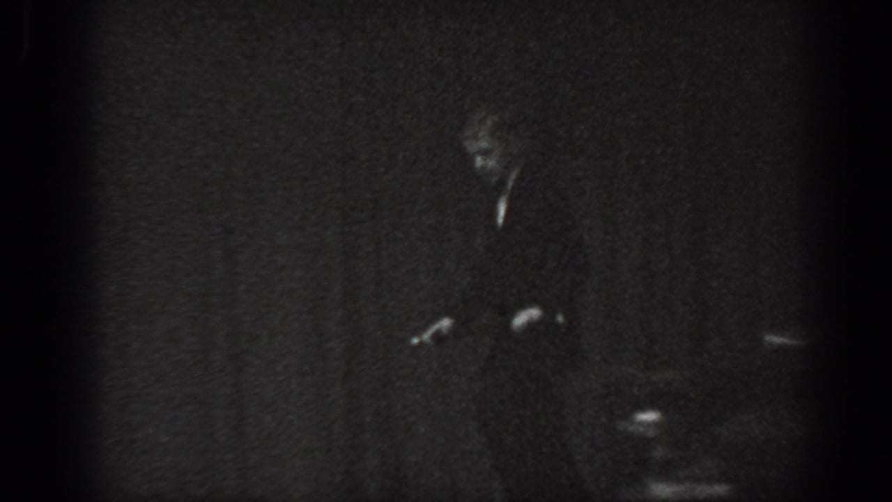 Cabaret performer in dark suit bent forward on a low-lit stage, Saint Louis, Missouri, 1965, 8mm film.