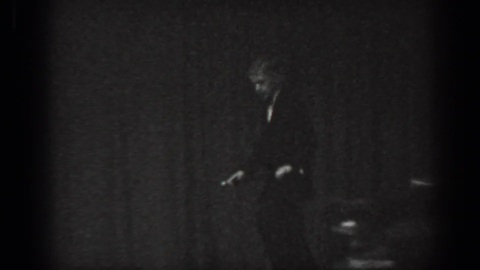 Cabaret performer in dark suit bent forward on a low-lit stage, Saint Louis, Missouri, 1965, 8mm film.
