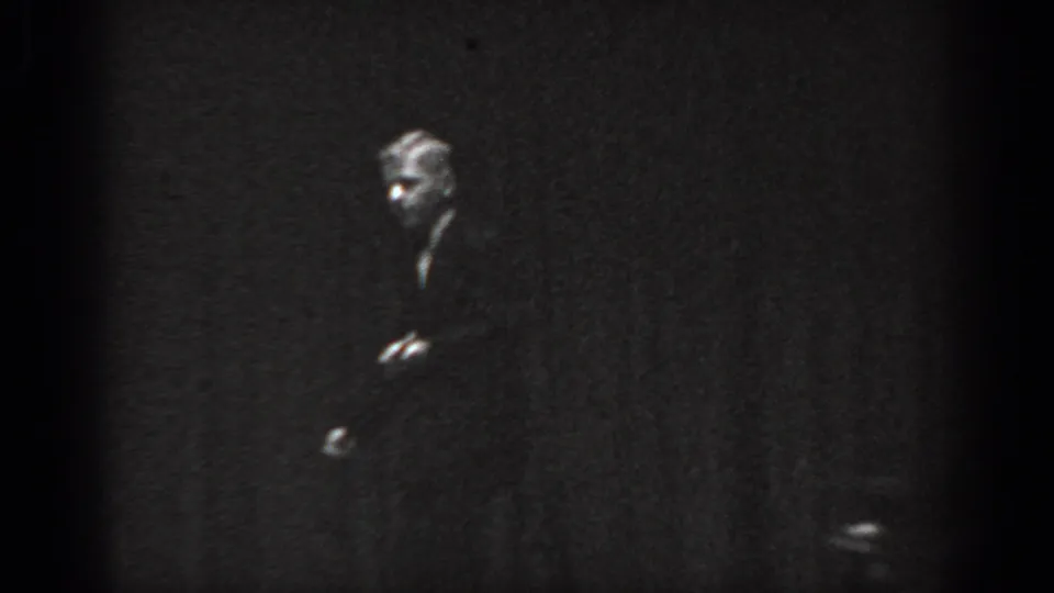 Cabaret performer in low crouching or side-leaning posture on dark stage, Saint Louis, Missouri, 1965, 8mm film.