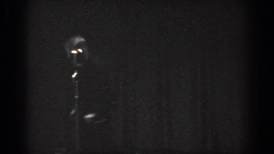Child tap dancer in movement on a low-lit stage beside a vintage microphone stand, circa 1965 8mm home movie, Saint Louis Missouri.