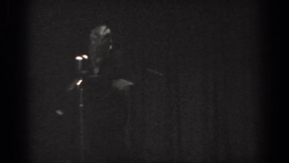 Grainy 8mm black-and-white frame circa 1965, performer at microphone on a dim stage, Saint Louis, Missouri.