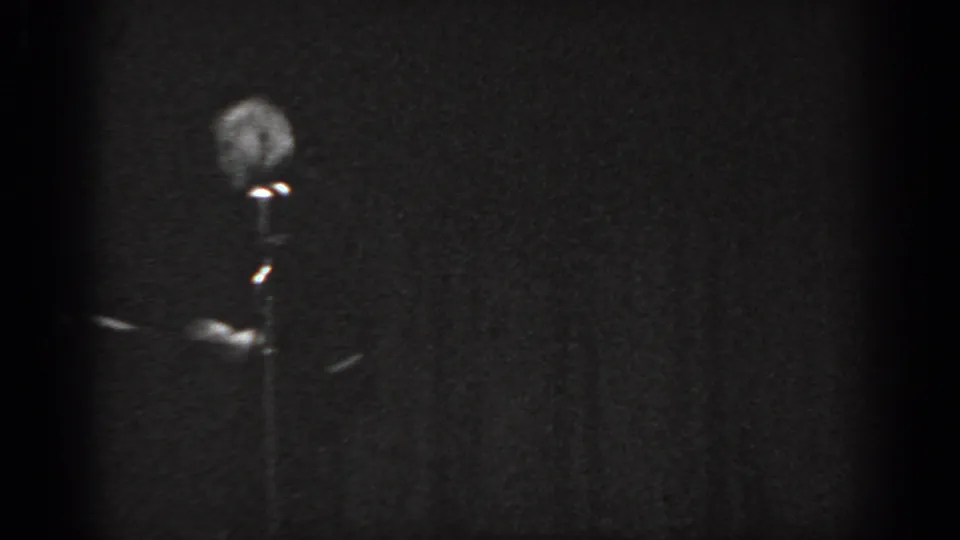 Near-silhouette 8mm frame circa 1965, figure barely discernible at microphone under severe underexposure, stage in Saint Louis, Missouri.