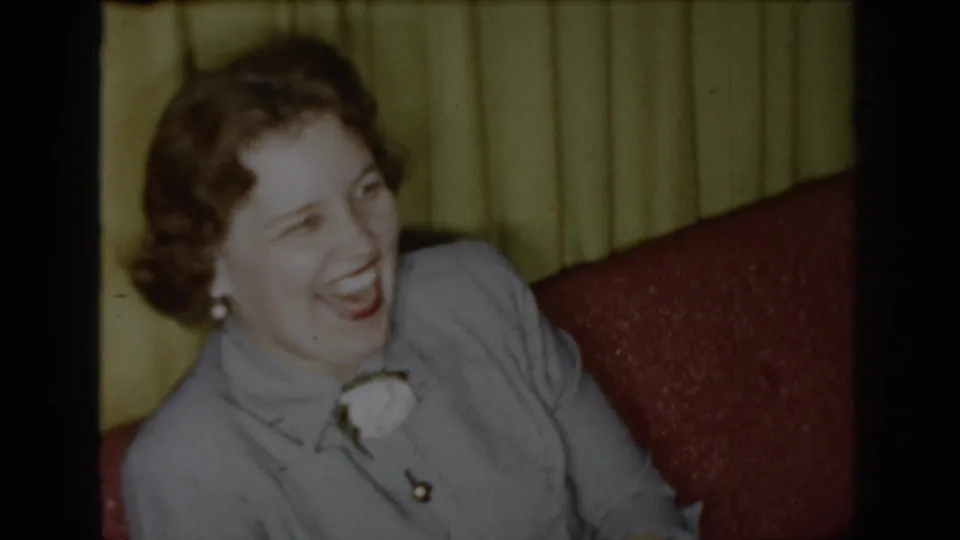 1965 Saint Louis 8mm frame of a woman laughing warmly while seated in a private interior.