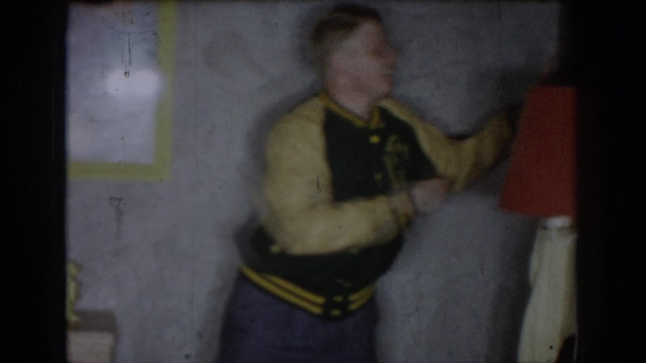 Motion-blurred figure in what appears to be a varsity-style jacket, opening frame of 8mm home movie, circa 1965, Saint Louis, Missouri.