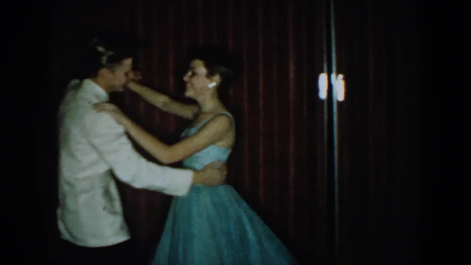 Teenage couple in formal attire, white dinner jacket and light blue strapless ballgown, dancing in close hold against a dark red curtain, 8mm home movie, 1965, Saint Louis, Missouri.