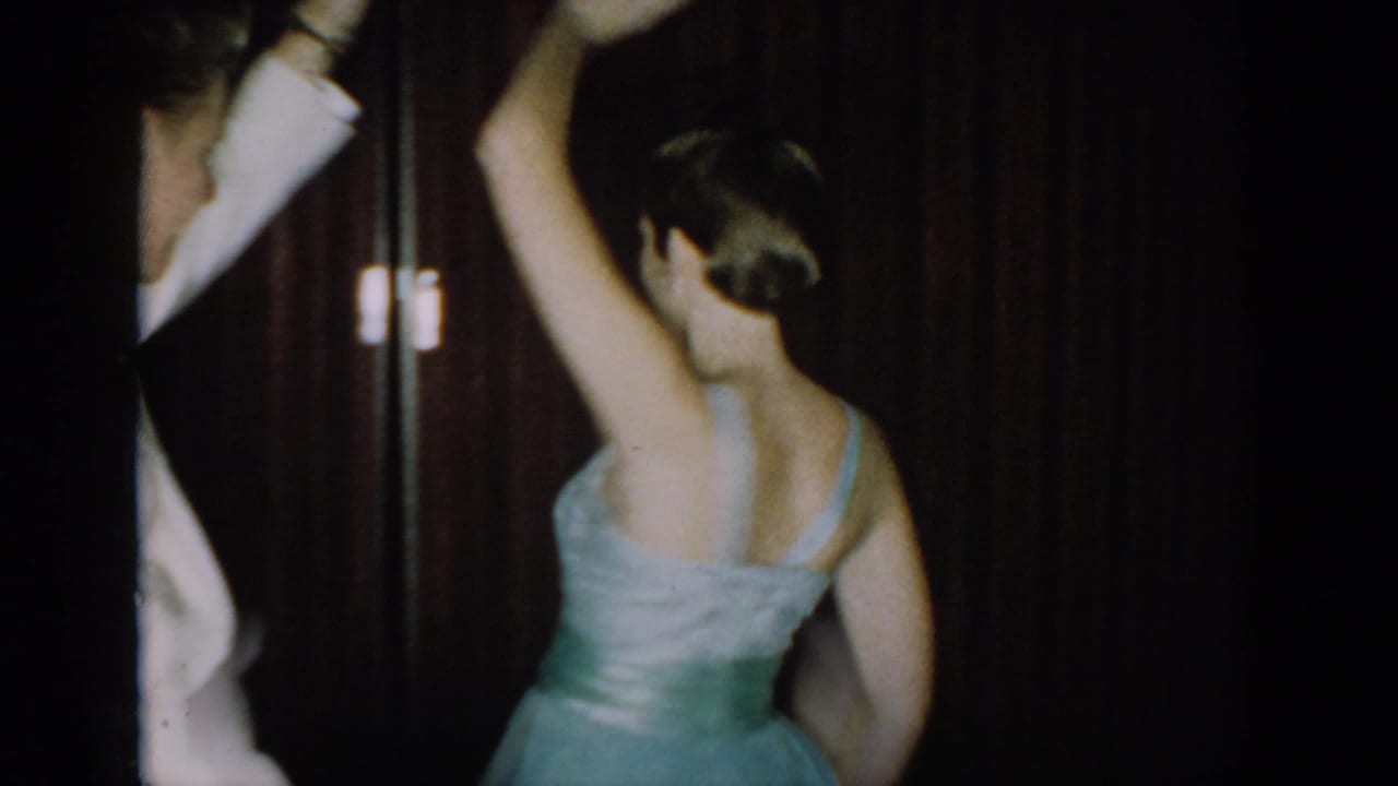 Woman in a light blue strapless gown with silver sash seen from behind, arm raised mid-spin at a mid-1960s formal party in Saint Louis, Missouri.