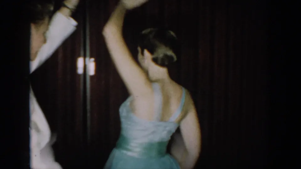 Woman in a light blue strapless gown with silver sash seen from behind, arm raised mid-spin at a mid-1960s formal party in Saint Louis, Missouri.