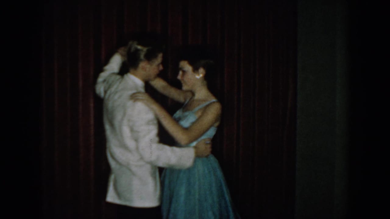Couple in close dance embrace in formal attire against a red curtain backdrop, 8mm home movie, Saint Louis Missouri, circa 1965.
