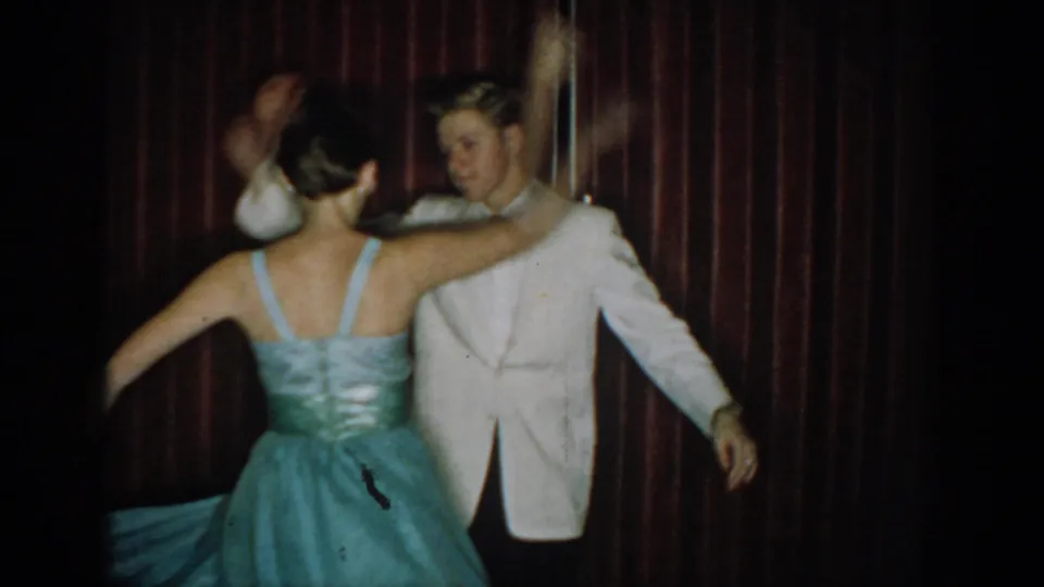 Rear view of dancing couple — woman's teal strapless gown shows fitted back detail, man in white jacket arm extended, 8mm home movie circa 1965.