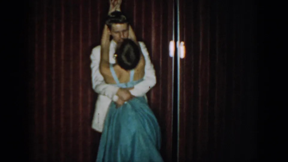 8mm home movie, circa 1965, Saint Louis: couple in close ballroom hold, woman's head tilted forward, small lamp visible at right edge of frame.