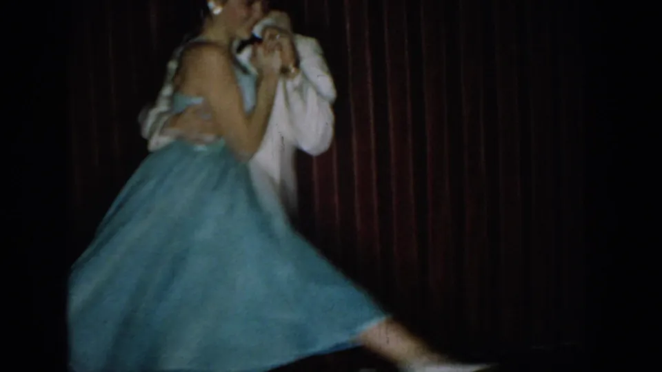 Dancing couple mid-spin, the woman's powder-blue skirt blurred with motion against a red velvet curtain, circa mid-1960s.
