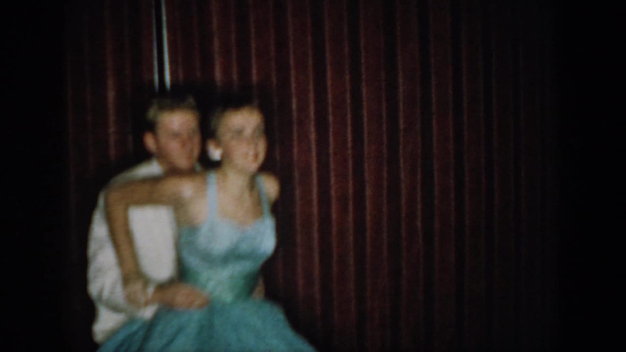 Young couple in 1960s formal attire pose before a dark red curtain — woman in light blue ball gown, man in white jacket — in what appears to be a mid-1960s Saint Louis social occasion.
